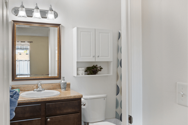 A neatly organized bathroom featuring a sink with a mirror, overhead lighting, and cabinetry above the toilet.