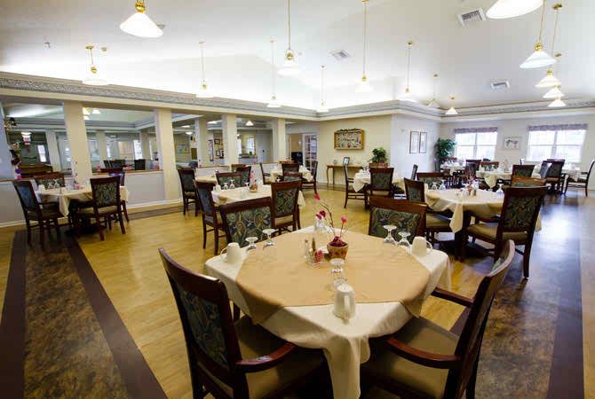 An elegantly set dining room with tables and chairs neatly arranged, featuring warm lighting and a wooden floor.