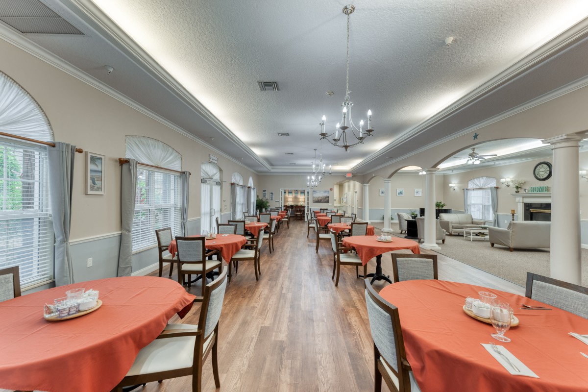 A spacious dining room with neatly arranged tables covered in orange tablecloths and elegant chandeliers hanging from the ceiling.