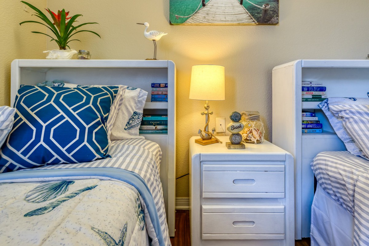 A cozy bedroom with a coastal-themed decor, featuring a nightstand, lamp, and decorative items.