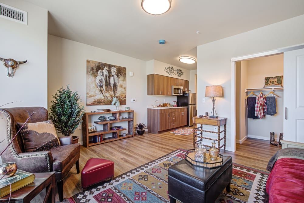 A cozy living area with a connected kitchen, featuring warm wood floors, comfortable seating, and decorative elements like artwork and an indoor plant.