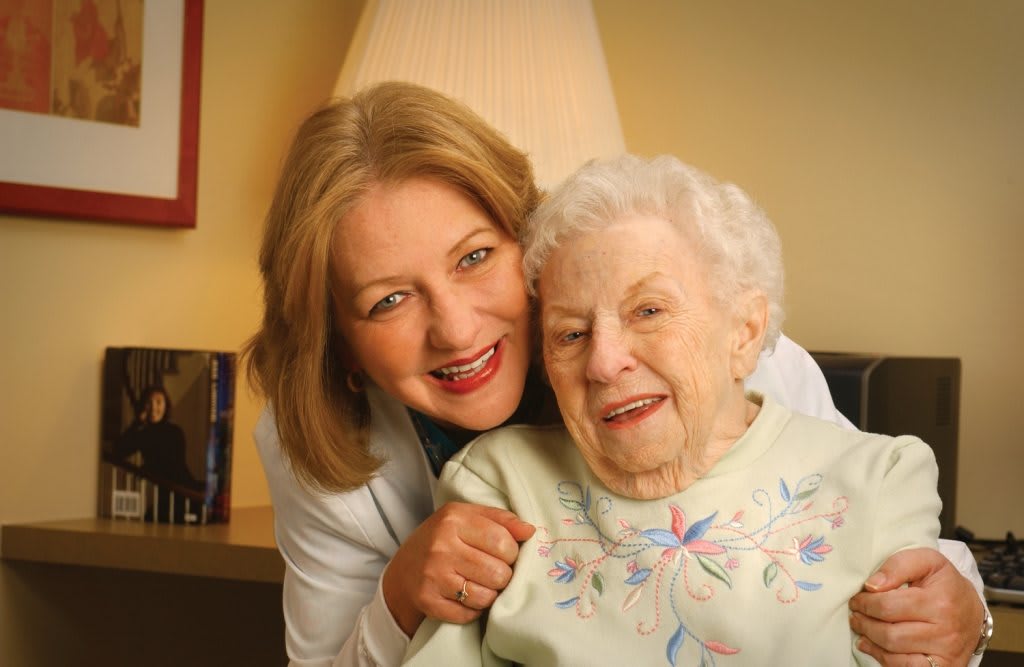 An elderly woman smiling with a caregiver indoors.