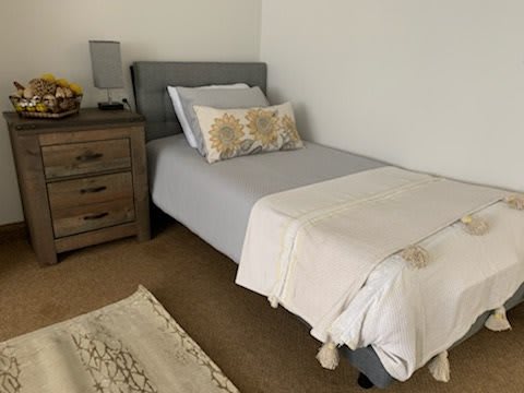 A minimalist bedroom featuring a neatly made bed with gray bedding and a decorative pillow, adjacent to a wooden nightstand.