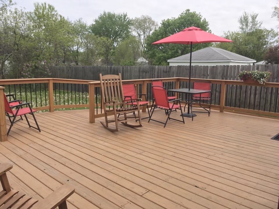 A spacious wooden deck featuring a dining set with an umbrella and two rocking chairs.