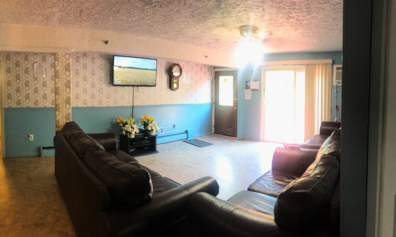 A cozy living room with sofas, a mounted television, and sunlight streaming through sliding doors.