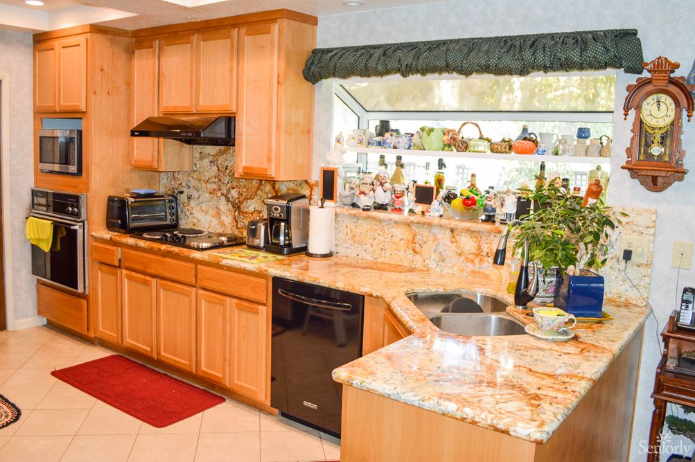 A cozy kitchen with wooden cabinets and a marble countertop, featuring various appliances and decorative items.