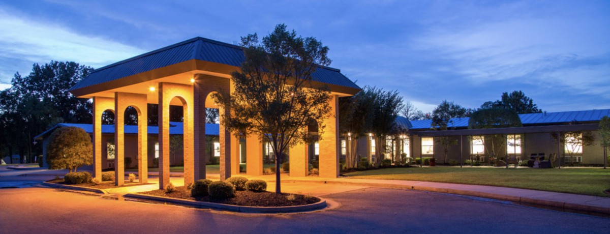 A well-lit building in the evening surrounded by trees.