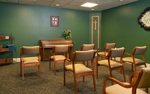 A small chapel with seating and an organ against a green wall featuring a cross.