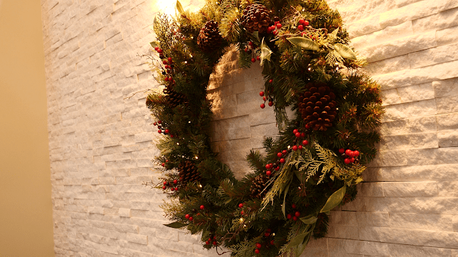 A festive wreath adorned with berries and pinecones hangs on a wall.