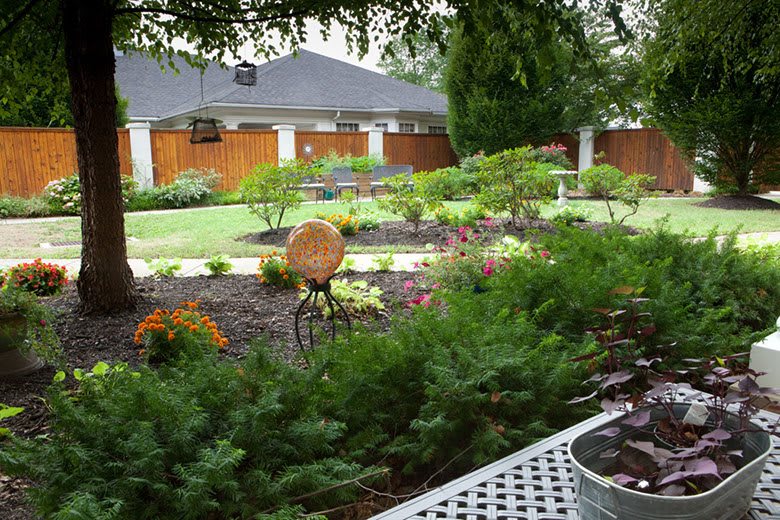 A beautifully landscaped garden with various flowers and greenery, enclosed by a wooden fence.