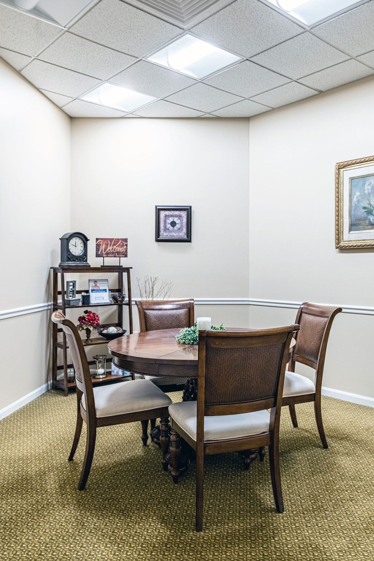 A small meeting room with a round table and four chairs, featuring a shelving unit and wall decorations.