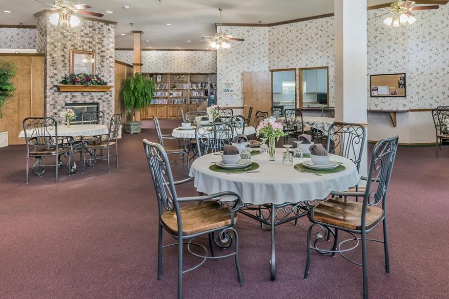 A cozy dining area featuring elegantly set tables with floral decorations, surrounded by stylish metal chairs.