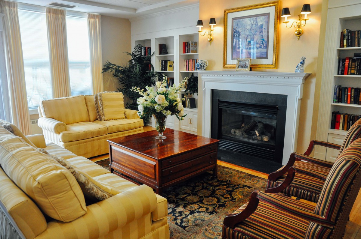 A cozy living room featuring a fireplace, yellow sofas, and a wooden coffee table adorned with flowers.