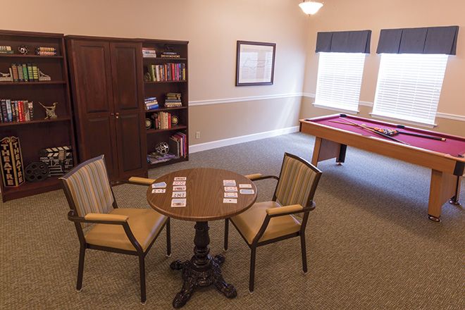 A cozy game room featuring a pool table, bookshelf, and a small table with chairs.
