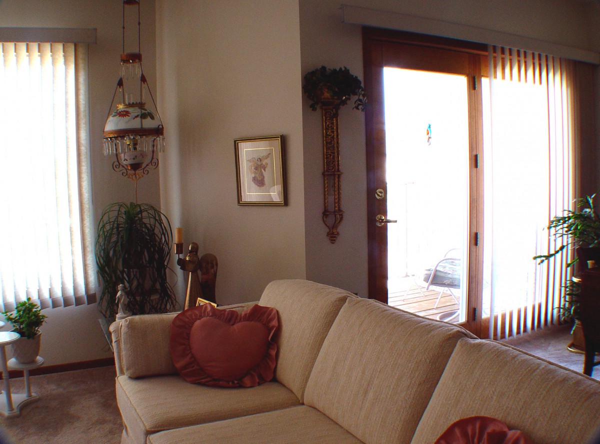 A cozy living room with a beige sofa and heart-shaped cushions, featuring decorative elements and a door leading outside.