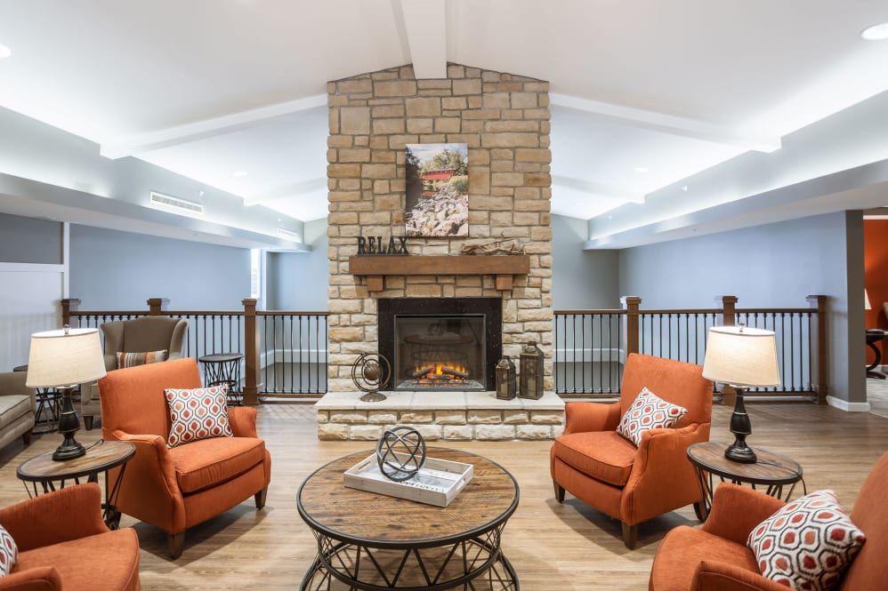 A cozy living room with a stone fireplace, orange chairs, and a wooden table.