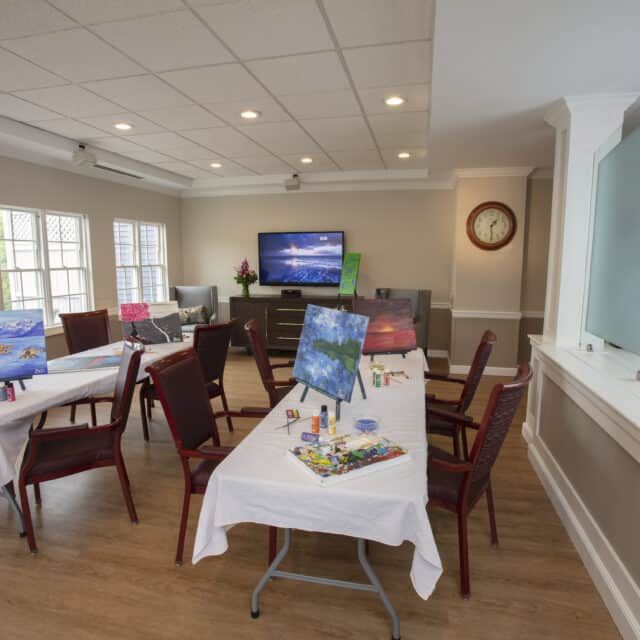 A well-lit meeting room with tables, chairs, and a television.