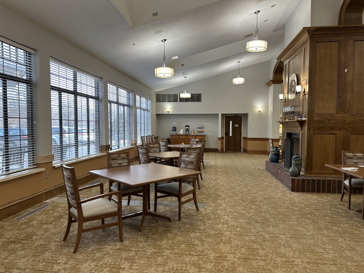 A spacious, carpeted room with tables and chairs, large windows, and a fireplace.