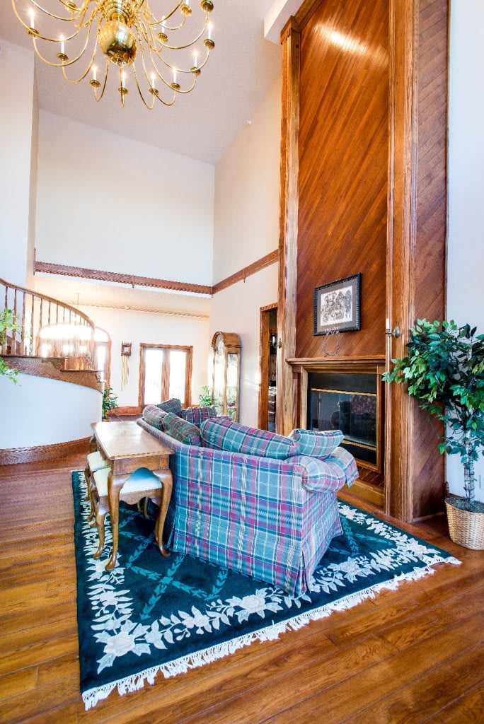 A spacious living room featuring a high ceiling, wooden accents, and a central fireplace, with a cozy seating area and staircase.