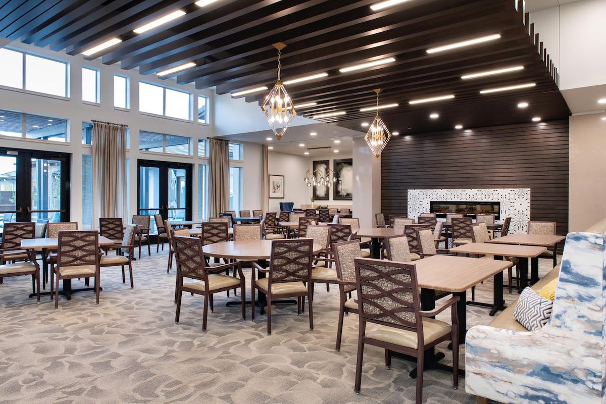 A modern dining area with arranged tables and chairs, featuring elegant lighting and large windows.