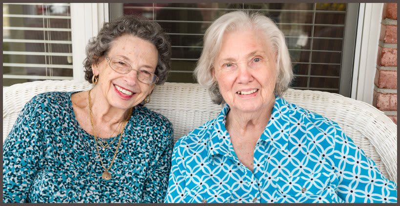 Two elderly women sitting together, smiling warmly.