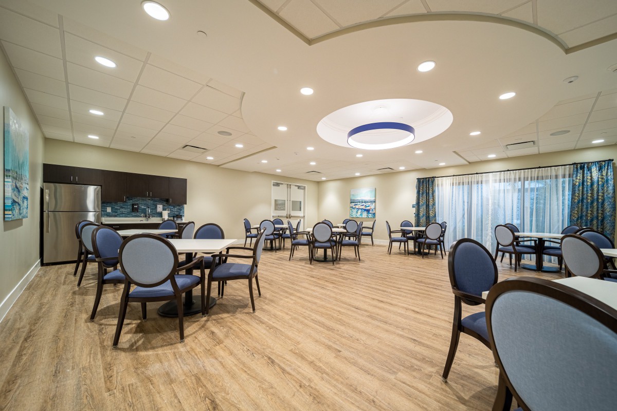 A modern dining room with neatly arranged tables and chairs, featuring elegant lighting and a wooden floor.