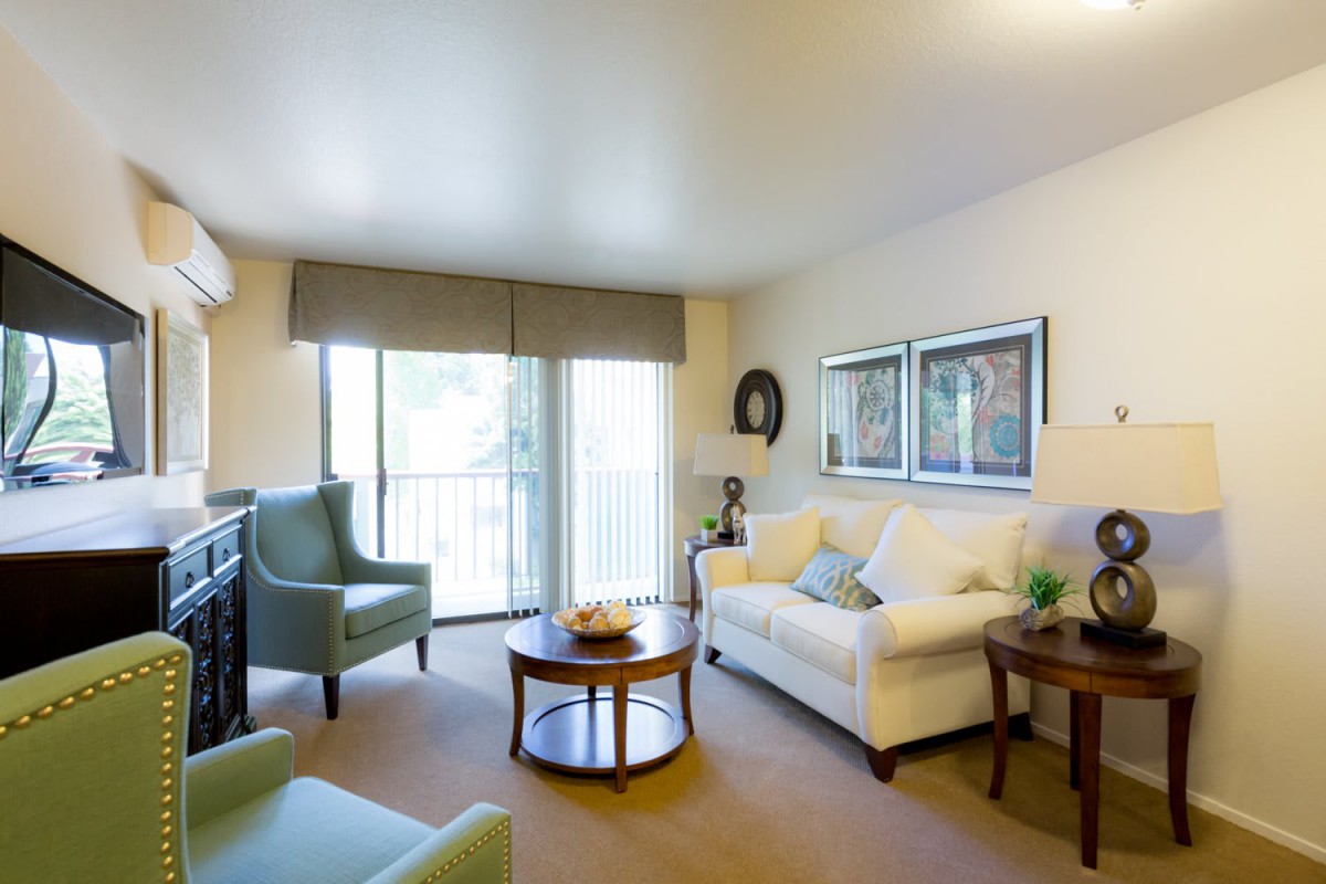 A cozy and well-decorated living room featuring a white sofa, blue chair, wooden coffee table, and art pieces on the wall.
