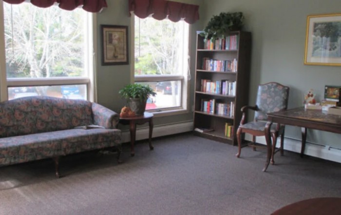 A cozy living room with a sofa, bookshelf, and large windows letting in natural light.