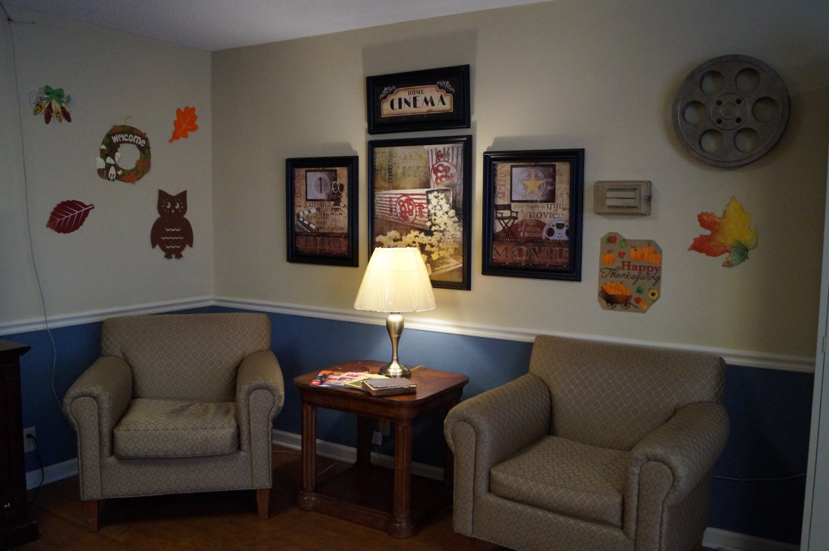 A cozy living room with two armchairs, a lamp on a wooden side table, and decorative wall art.