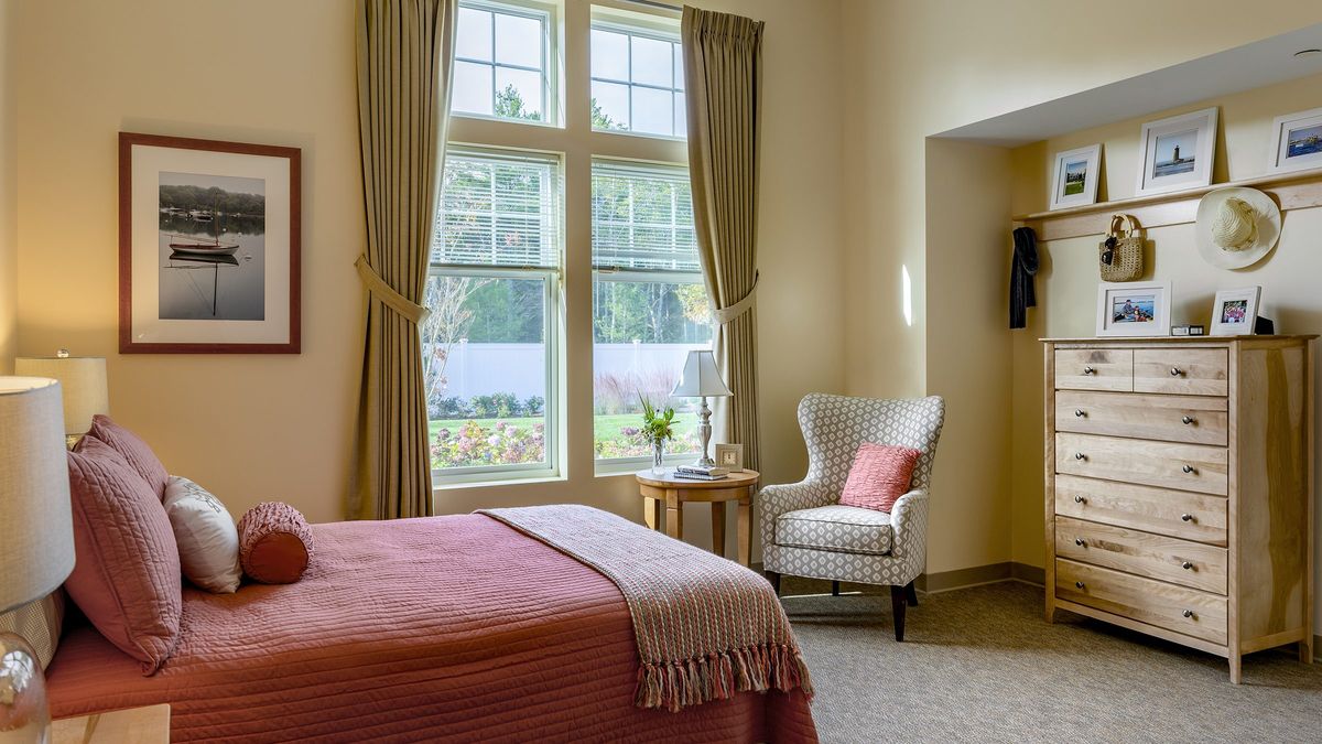 A cozy bedroom with a large window, allowing natural light to fill the space, decorated with an armchair and stylish curtains.