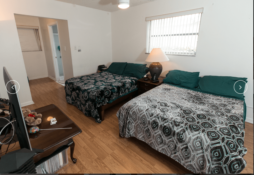 A cozy bedroom featuring two beds with patterned covers, a wooden floor, and a lamp on a bedside table.
