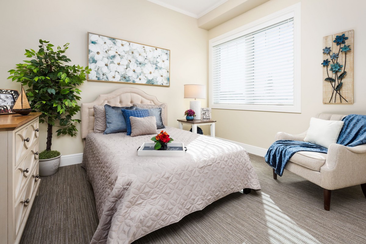 A cozy and elegantly decorated bedroom with a neatly made bed, artwork on the wall, plant, and natural light streaming through the window.