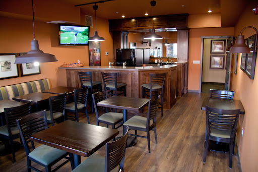 A cozy dining area showcasing wooden tables and chairs, with a bar in the background and sports on the TV.