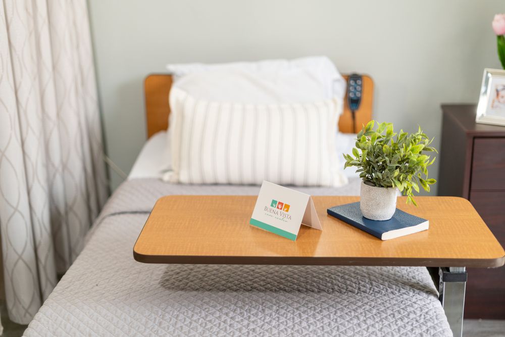 A cozy bed setup with a pillow, a tray table holding a plant and a card, alongside a book.