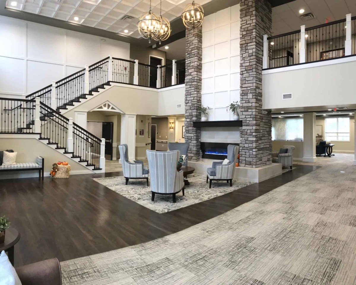 A spacious and elegant lobby featuring a grand staircase, comfortable seating area, and a central fireplace.