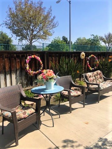 A cozy outdoor patio setup with wicker chairs, a small round table, and floral decorations under the sunny sky.