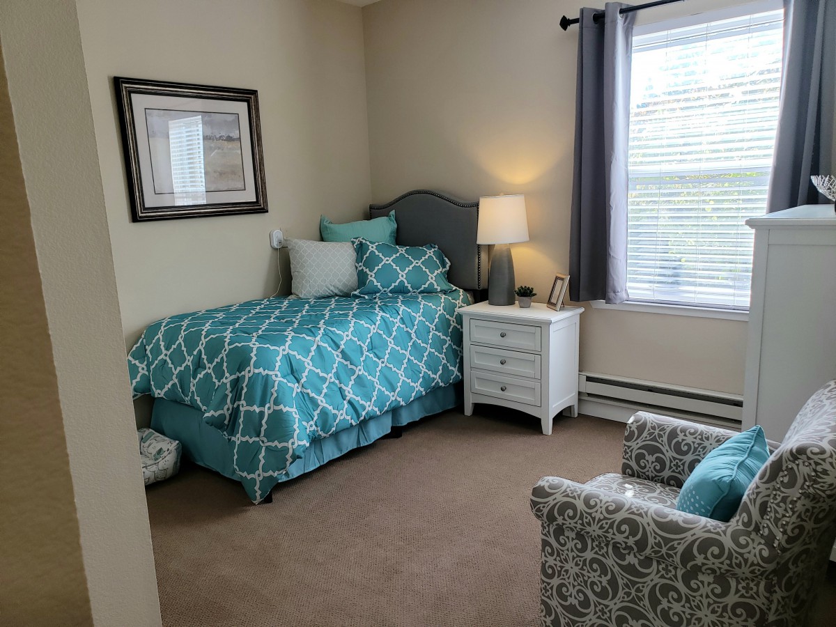 A cozy bedroom with teal bedding, a nightstand, and an armchair by the window.