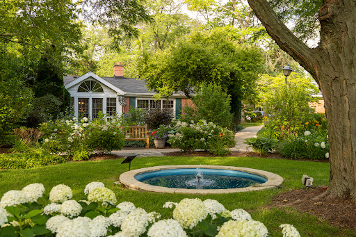 A serene garden scene featuring a charming house, vibrant flowers, and a peaceful water feature.