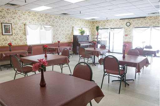 A spacious dining area featuring neatly arranged tables, chairs, and decorative flowers, with a piano in the background.