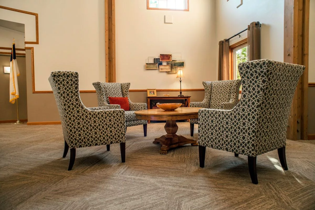 A modern living room with patterned armchairs surrounding a wooden coffee table, featuring neutral tones and wood flooring.