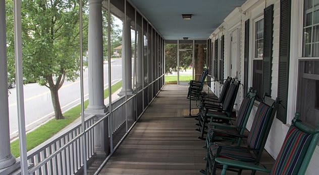 A serene screened porch with rocking chairs and columns overlooking a green lawn.