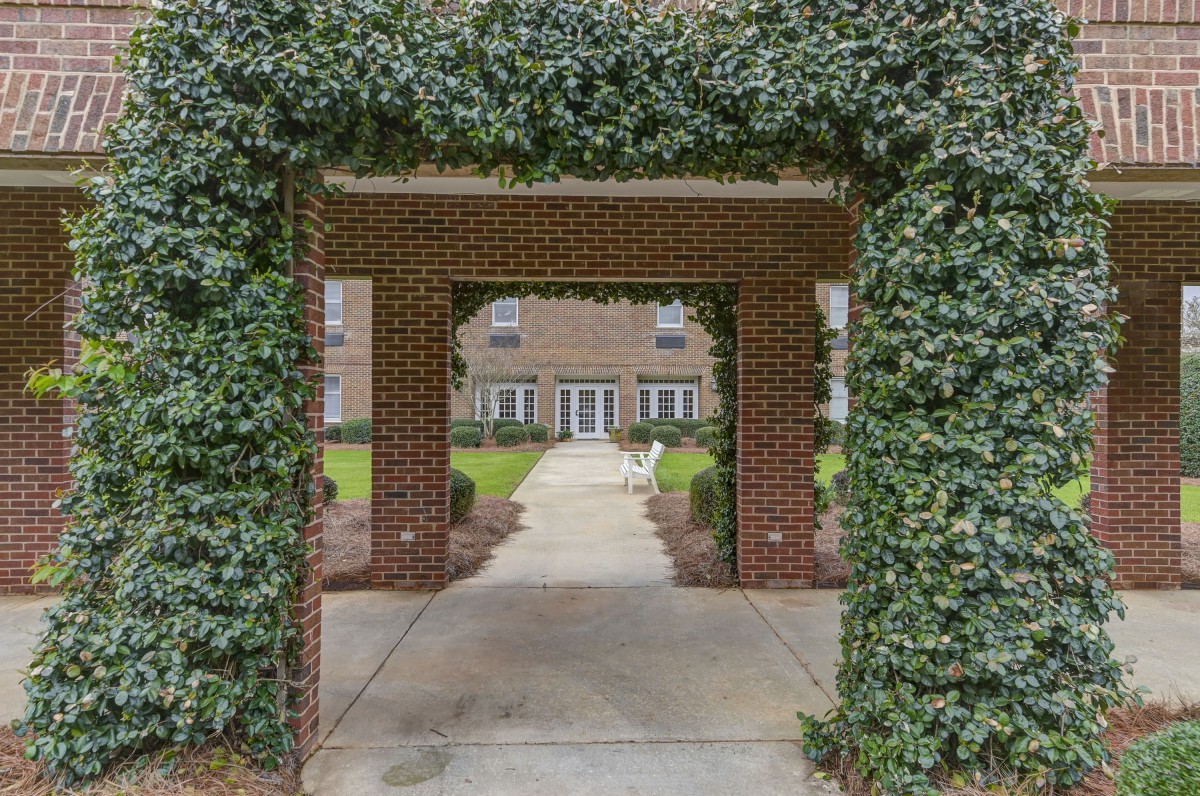 A brick archway covered in ivy leads to a pathway and a building in the background.
