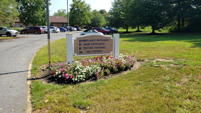 Entrance sign with parking directions surrounded by flowers and greenery.