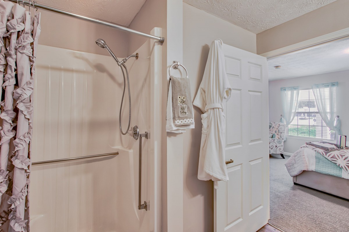 A view of a bathroom featuring a shower with a grab bar, towels, and a robe hanging on the door.