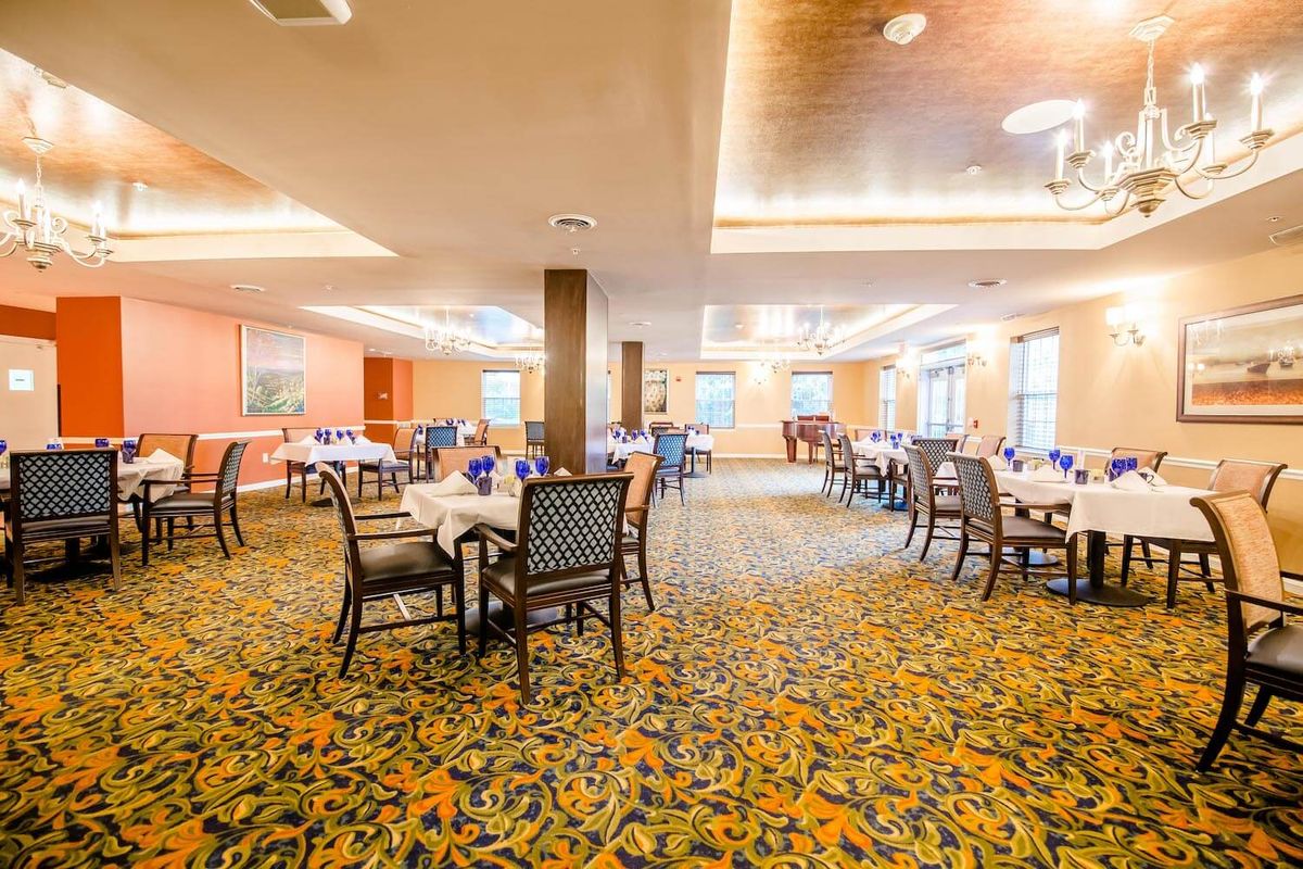 A spacious dining room with neatly arranged tables and chairs, featuring vibrant carpeting and modern lighting.
