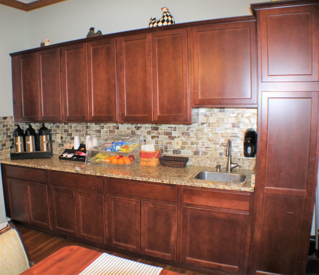 A kitchen with dark wood cabinets and a colorful tile backsplash, featuring a countertop with a sink and coffee station.