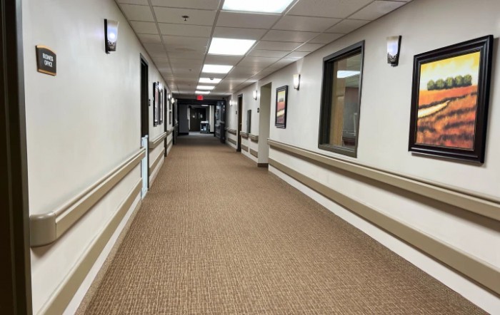 An empty, well-lit hallway with carpet flooring and framed pictures on the walls.