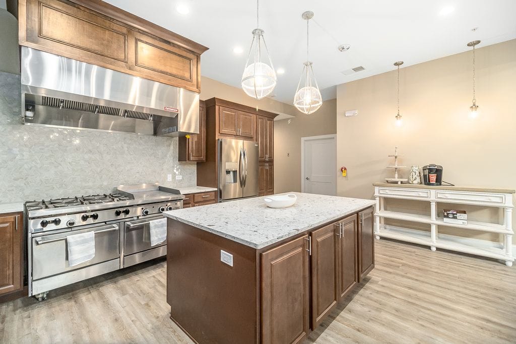 A modern kitchen featuring a central island with marble countertops, pendant lighting, wood cabinets, and stainless steel appliances.