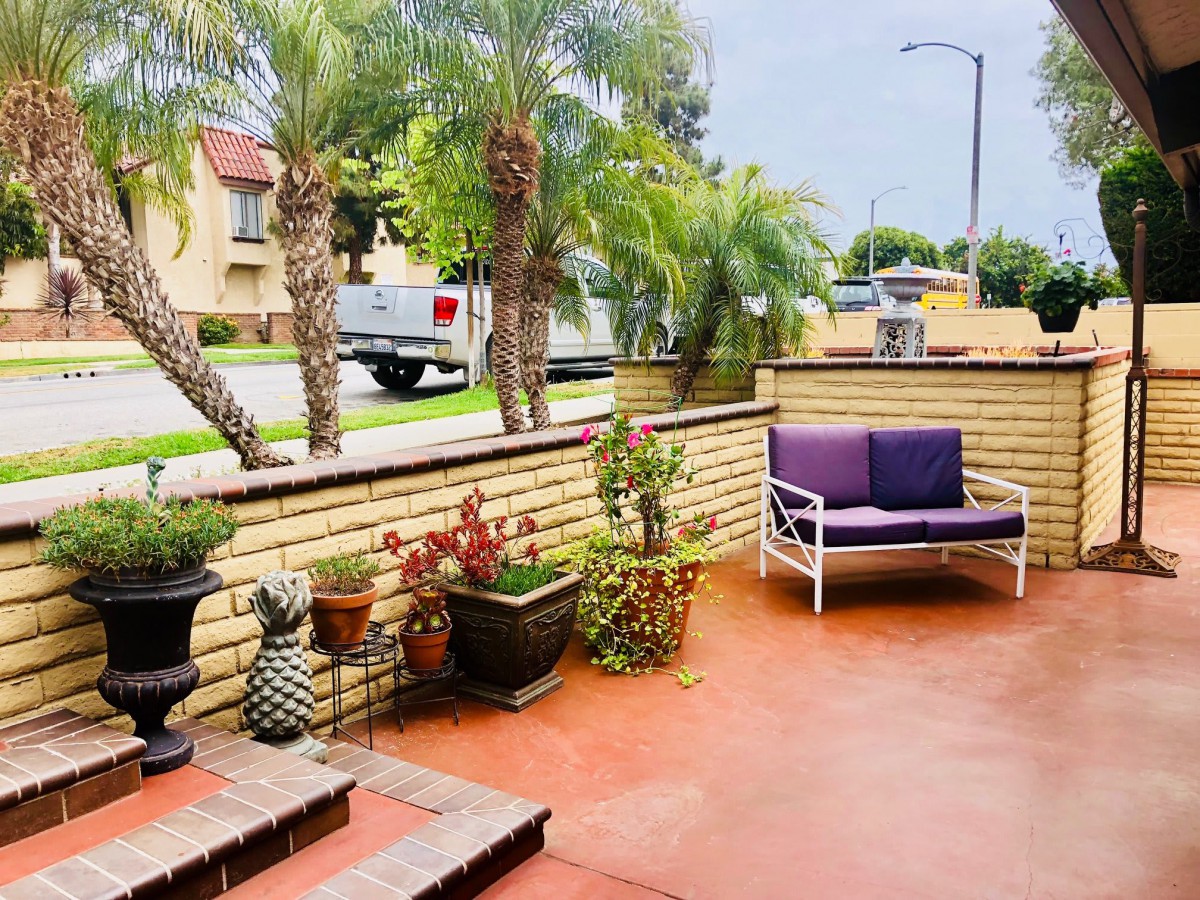 A cozy outdoor patio with plants and seating overlooking a street lined with palm trees.