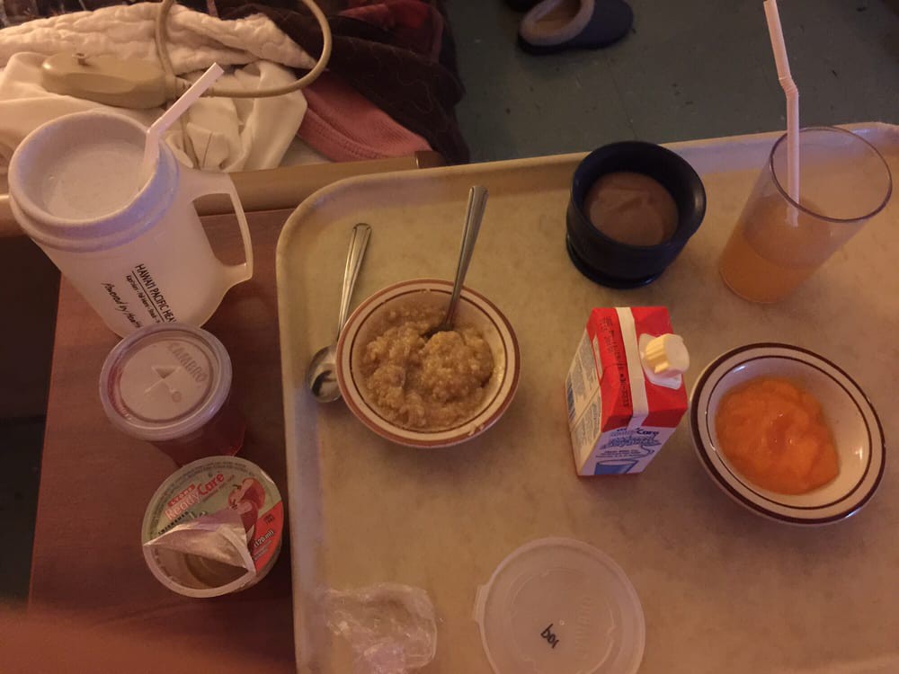 A hospital meal tray with oatmeal, a beverage, and juice.